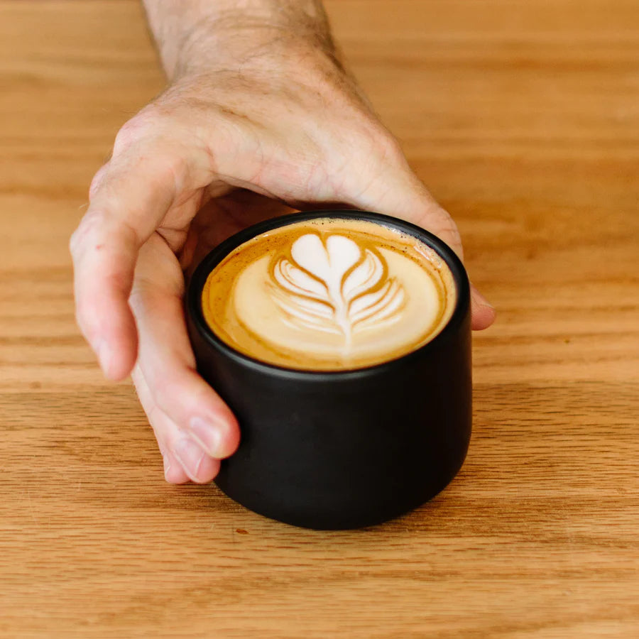 Latte art poured in a Fellow's black double wall ceramic cup